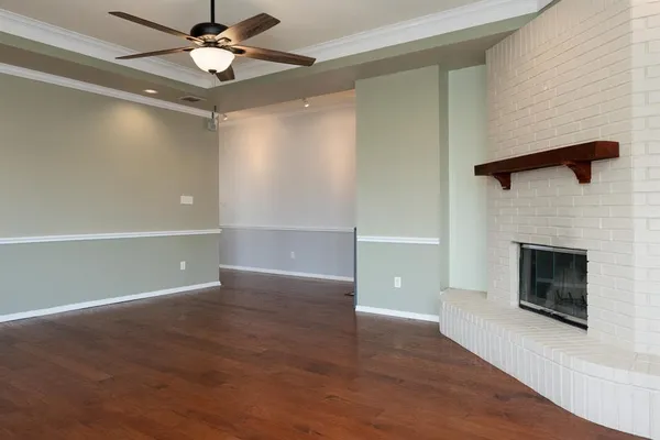 an empty room with wooden floor a ceiling fan a fireplace and windows