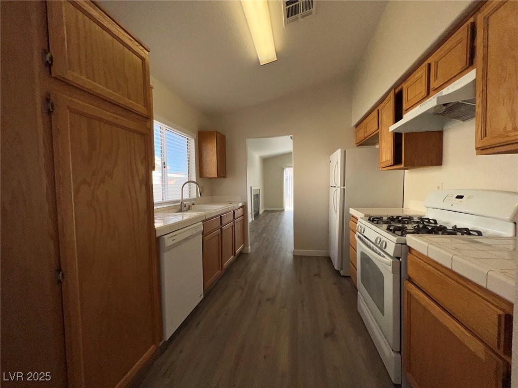 635 Delorean Drive North Las Vegas, NV 89081 - Photo 4 of 22 Kitchen featuring white appliances, tile counters, under cabinet range hood, dark wood-style floors, and brown cabinets