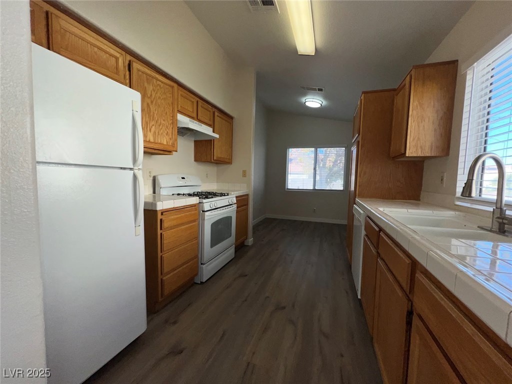 635 Delorean Drive North Las Vegas, NV 89081 - Photo 5 of 22 Kitchen featuring tile countertops, white appliances, vaulted ceiling, dark wood-type flooring, and under cabinet range hood