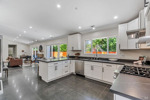 a kitchen with stainless steel appliances a sink a stove a refrigerator and white cabinets
