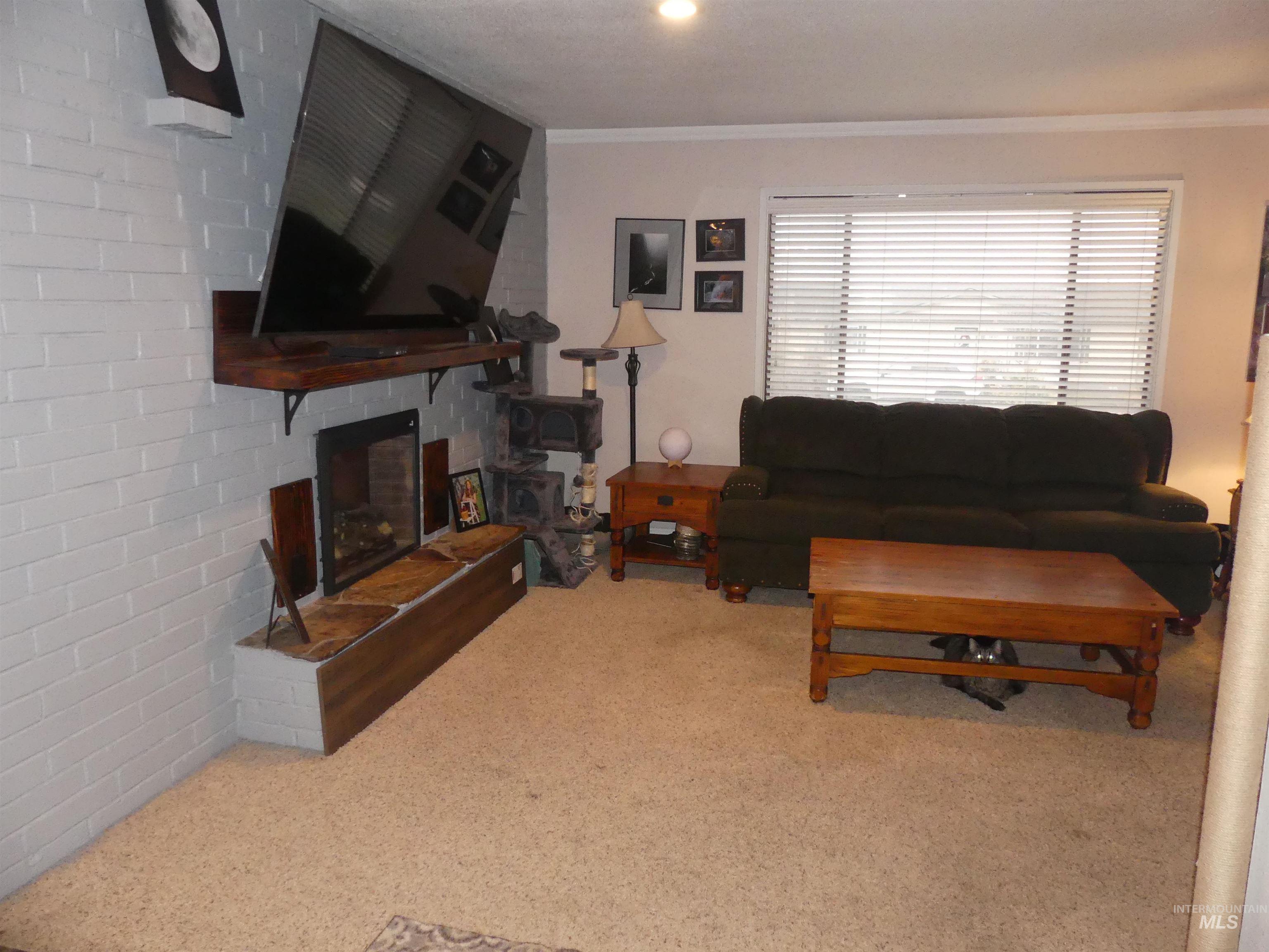 3427 18th Street Lewiston, ID 83501 - Photo 26 of 45 Carpeted living room featuring a fireplace, crown molding, and brick wall