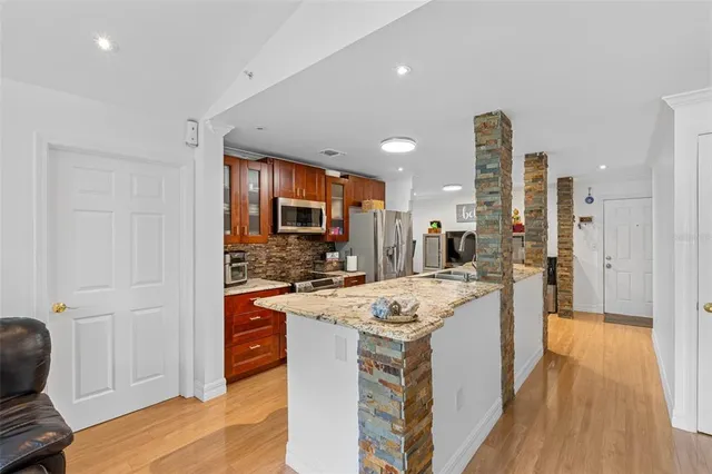 a kitchen with stainless steel appliances granite countertop a stove top oven a sink dishwasher and a refrigerator with wooden floor