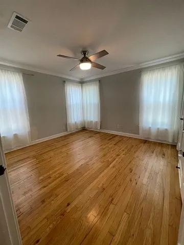 an empty room with wooden floor chandelier fan and windows