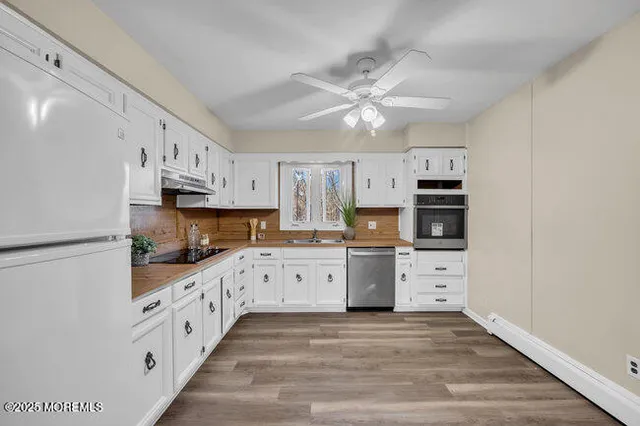 a kitchen with granite countertop a refrigerator oven a sink dishwasher and white cabinets with wooden floor