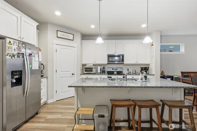 a kitchen with stainless steel appliances granite countertop a dining table chairs refrigerator and microwave