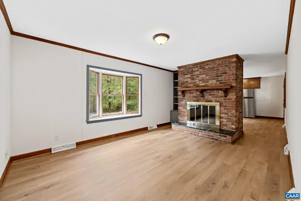 a view of an empty room with wooden floor fireplace and a window