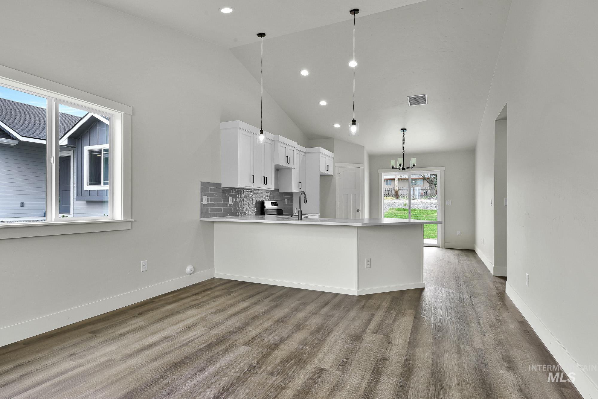 328 Packer Lane Homedale, ID 83628 - Photo 6 of 25 Kitchen featuring white cabinets, decorative backsplash, a peninsula, lofted ceiling, and suspended lighting