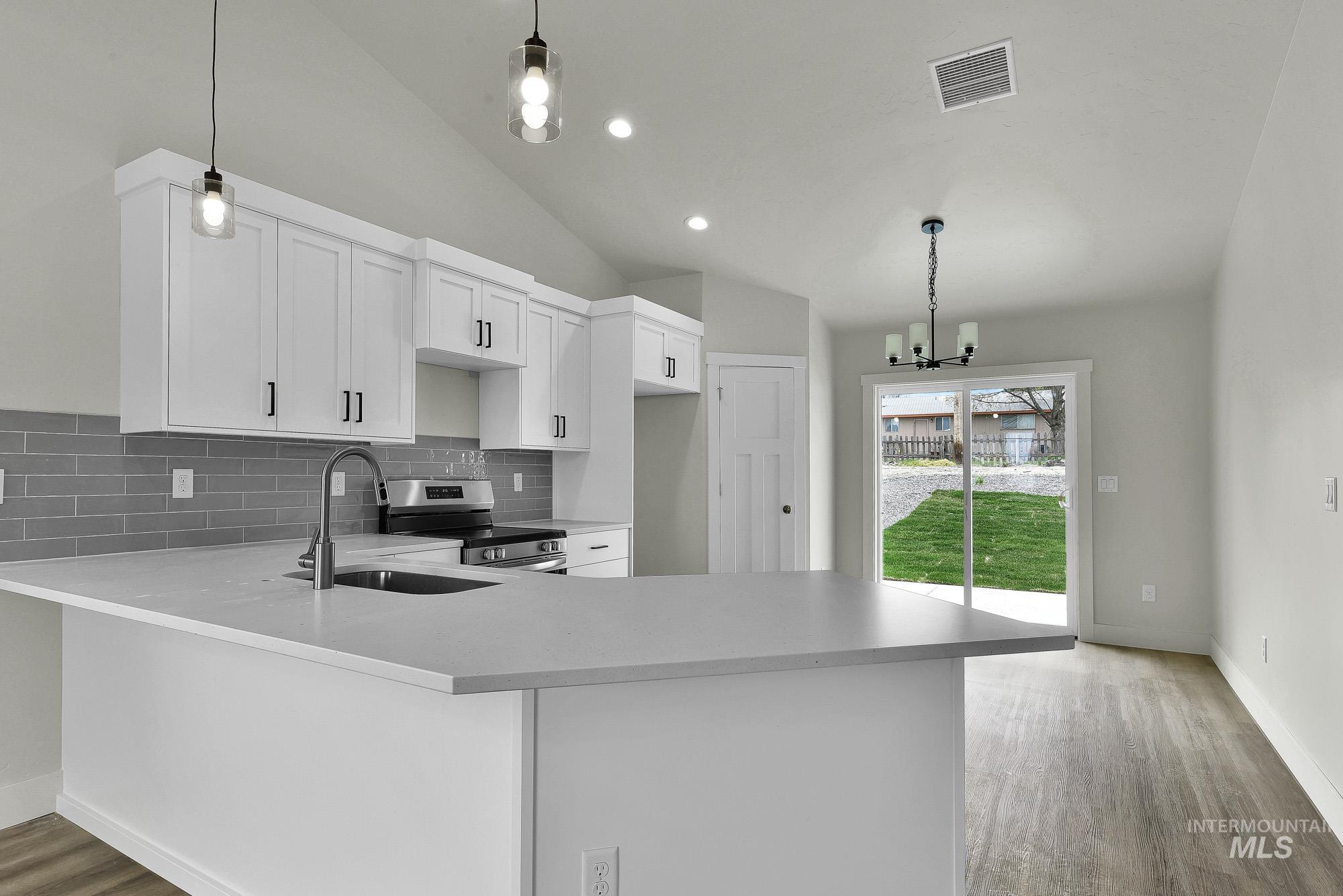 328 Packer Lane Homedale, ID 83628 - Photo 7 of 25 Kitchen featuring a peninsula, lofted ceiling, suspended lighting, decorative backsplash, and white cabinets