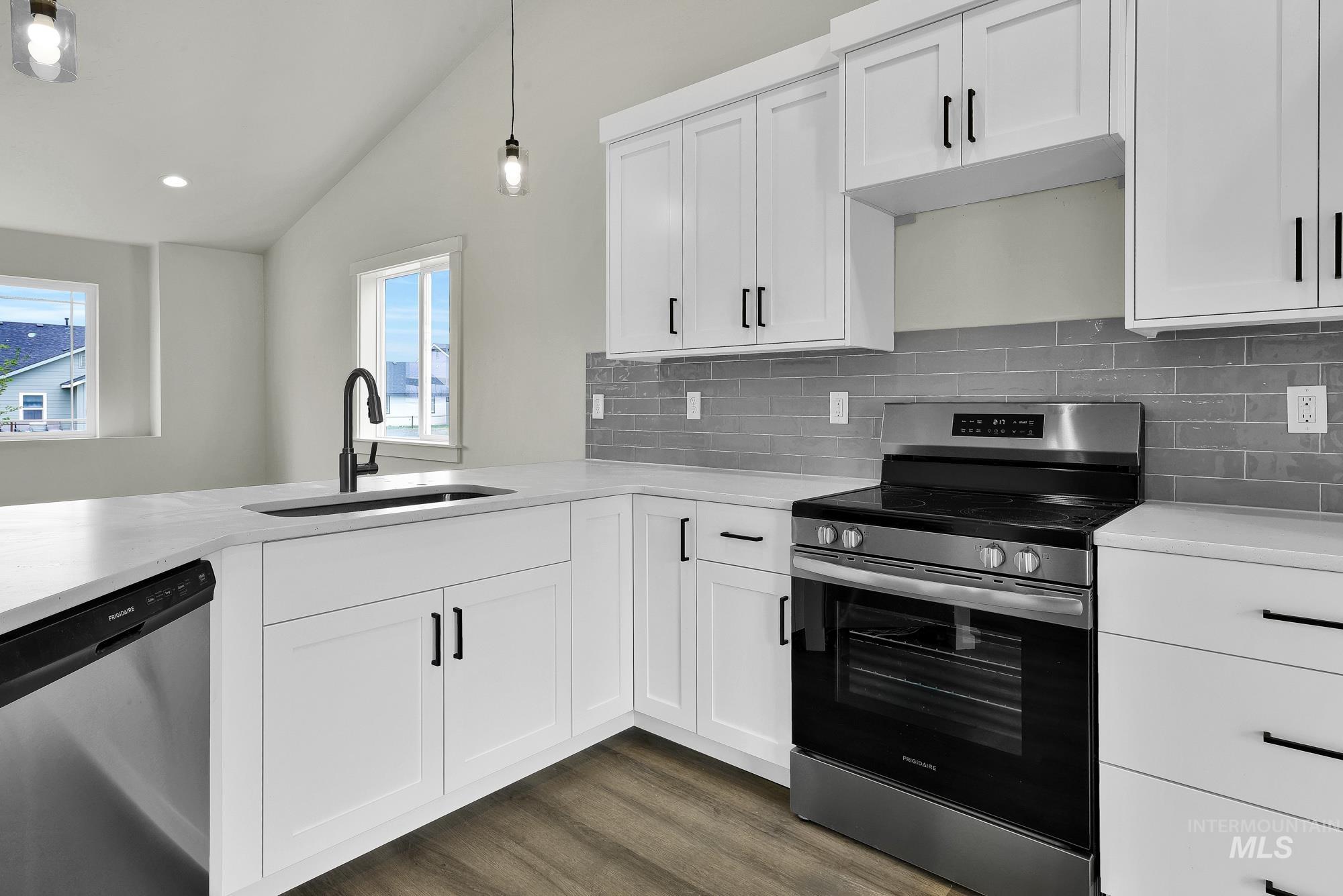 328 Packer Lane Homedale, ID 83628 - Photo 10 of 25 Kitchen featuring stainless steel appliances, lofted ceiling, white cabinetry, decorative backsplash, and hanging light fixtures