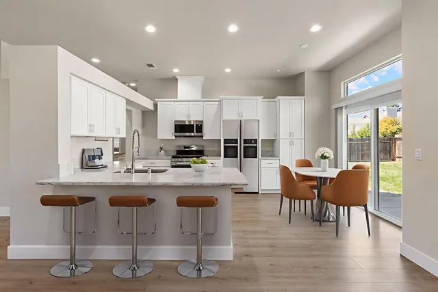 a kitchen with stainless steel appliances granite countertop a stove top oven a sink a dining table and chairs