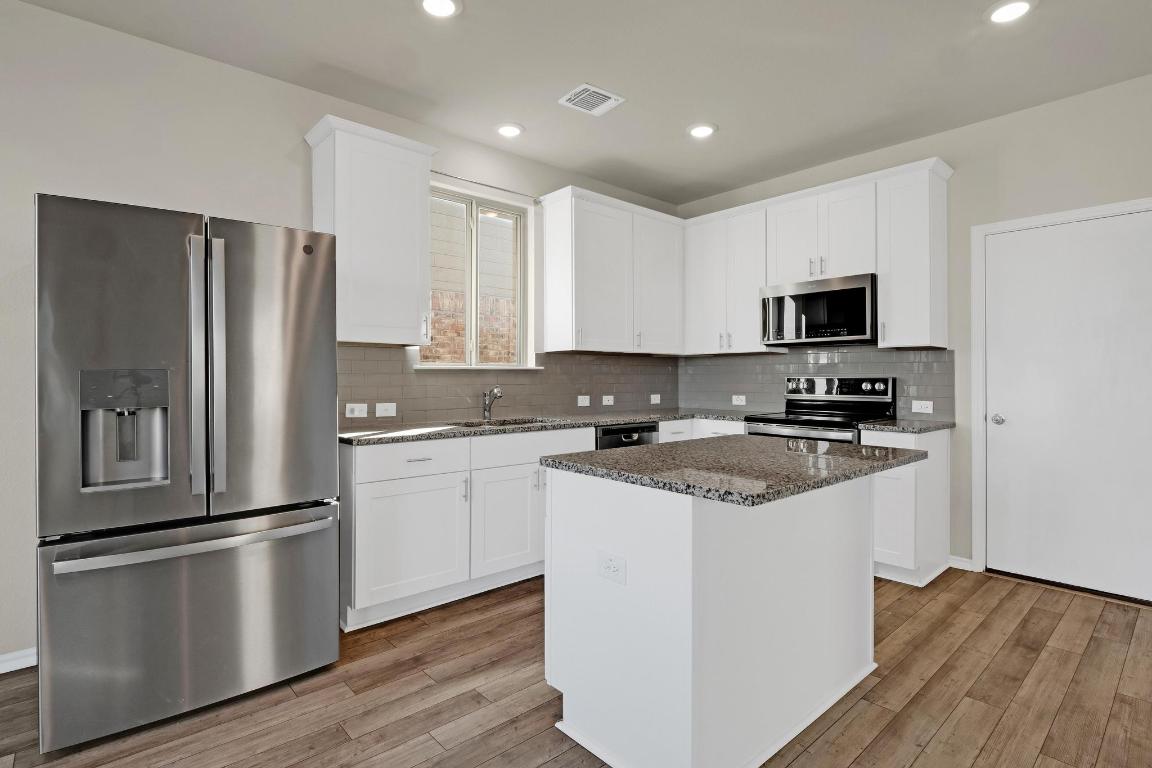 449 Stone Water Lane Jarrell, TX 76537 - Photo 5 of 21 a kitchen with stainless steel appliances granite countertop a refrigerator stove a sink and white cabinets with wooden floors