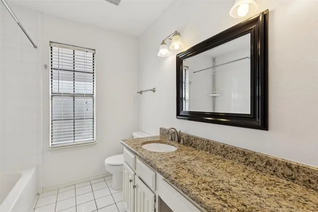 a bathroom with a granite countertop sink vanity mirror and toilet