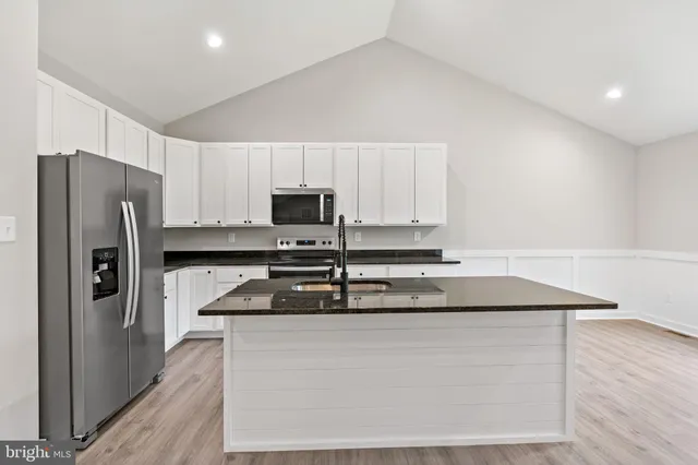 a kitchen with stainless steel appliances granite countertop a refrigerator a stove a sink and white cabinets