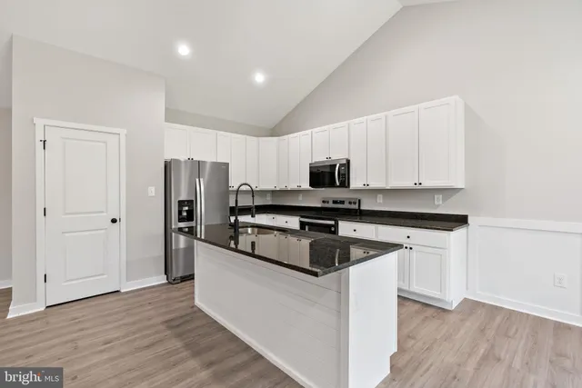 a kitchen with stainless steel appliances granite countertop a refrigerator a stove a sink and white cabinets with wooden floor