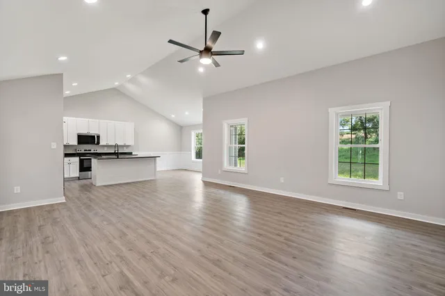 an empty room with wooden floor kitchen view and windows