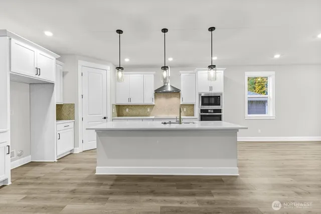 a large kitchen with stainless steel appliances kitchen island granite countertop a stove a sink a refrigerator and white cabinets with wooden floor