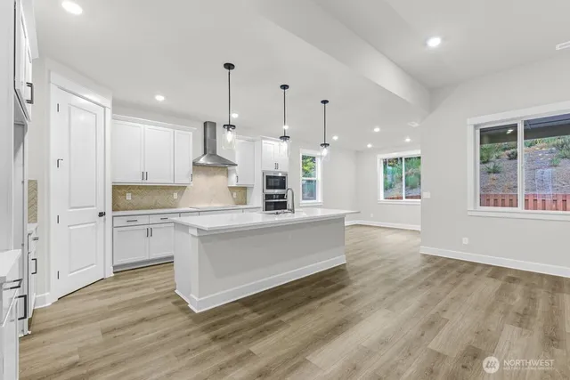 a large kitchen with granite countertop a stove a sink a refrigerator and white cabinets with wooden floor