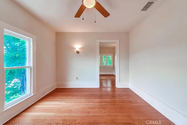 an empty room with wooden floor chandelier fan and windows