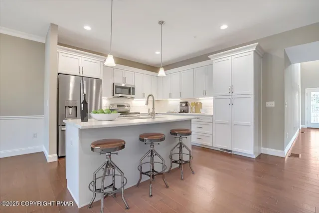 a kitchen with stainless steel appliances granite countertop a refrigerator a sink dishwasher a stove and white cabinets with wooden floor