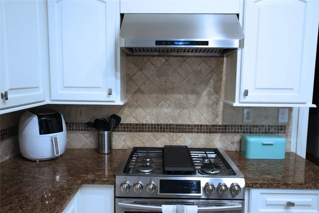 a kitchen with granite countertop a stove and white cabinets