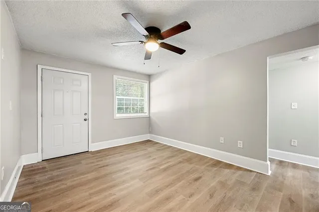 a view of an empty room with wooden floor and a ceiling fan