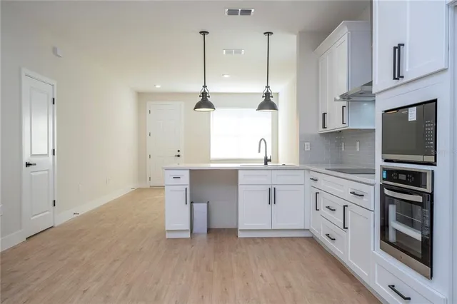 a kitchen with stainless steel appliances granite countertop a stove a sink and white cabinets with wooden floor