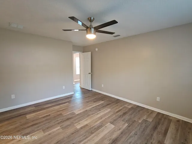 a view of an empty room with wooden floor and a ceiling fan