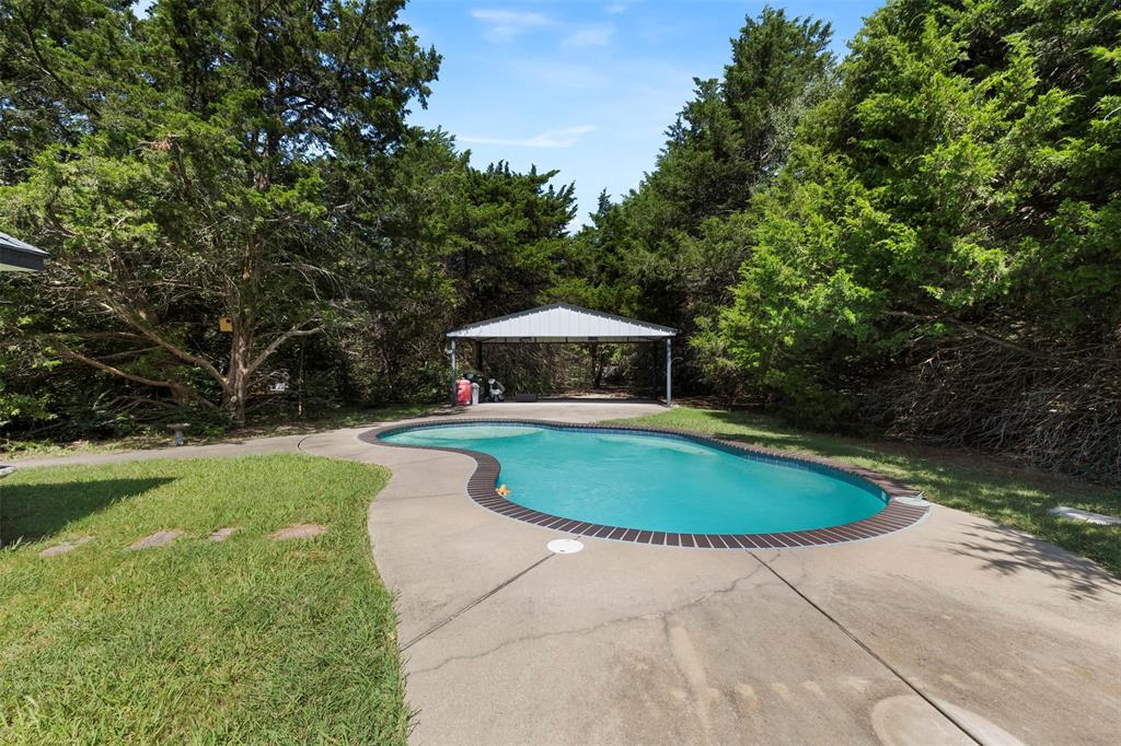 401 Rugged Drive Red Oak, TX 75154 - Photo 3 of 40 Freeform swimming pool with a brick coping and concrete surround, bordered by mature trees