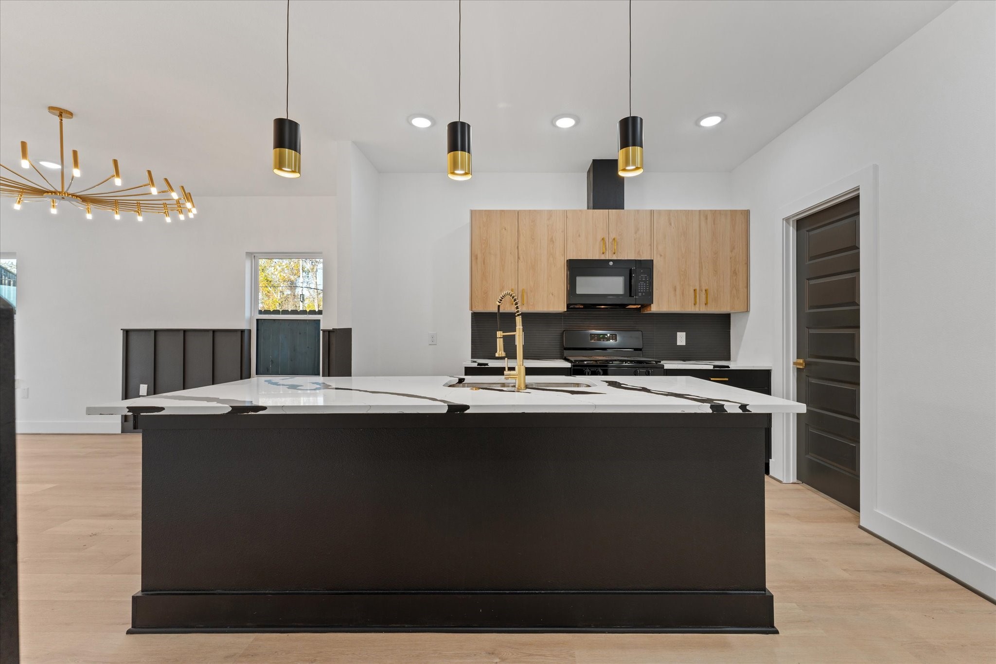 1010 Calvin Street Houston, TX 77088 - Photo 14 of 20 Sleek black cabinetry contrasts with warm wood accents. Equipped with stylish pendant lights and a chic chandelier, the space offers an open, airy feel with light flooring. Photos are from builders previously built model, same floor plan and finishes.