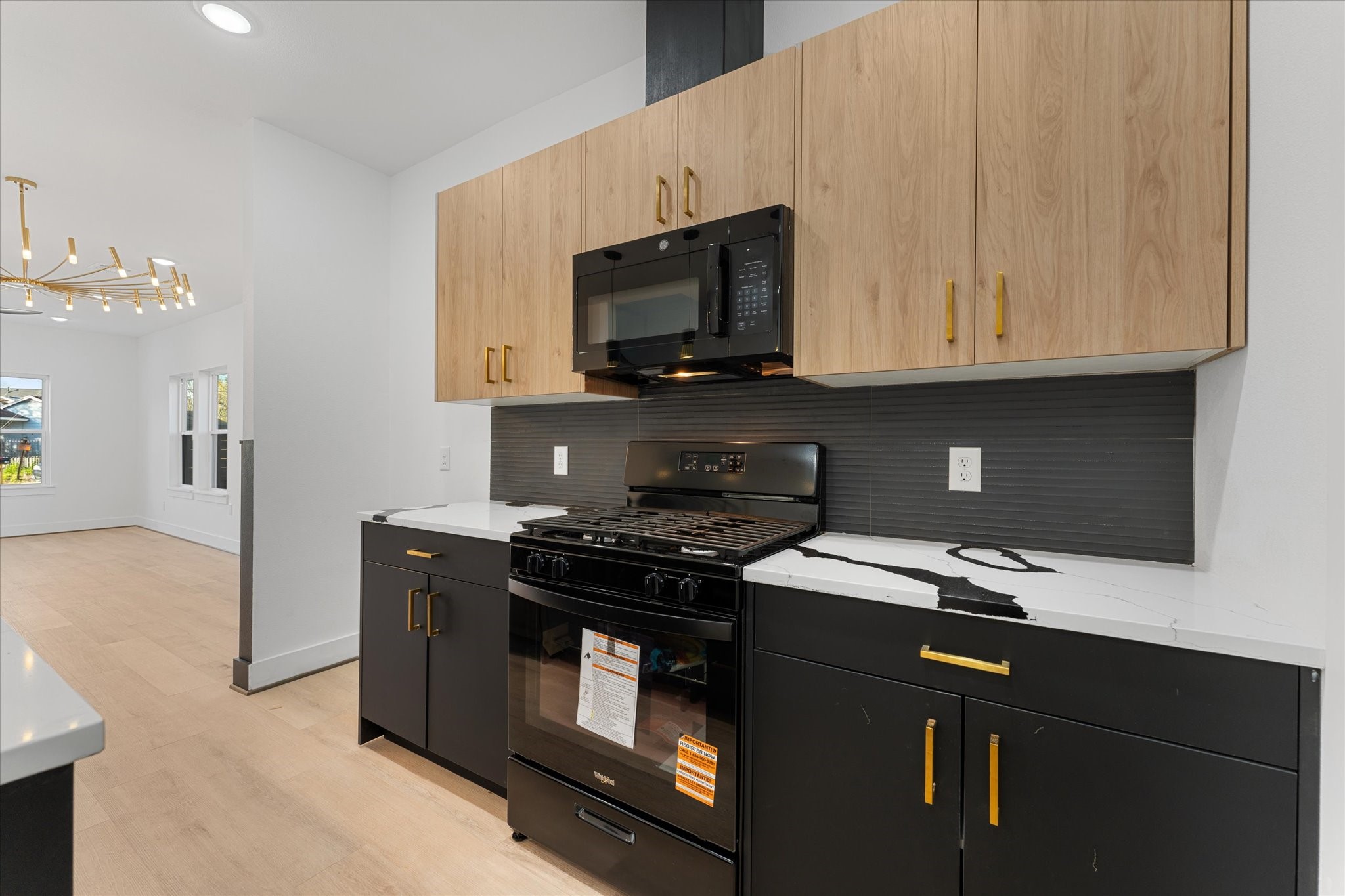 1010 Calvin Street Houston, TX 77088 - Photo 11 of 20 Modern kitchen features sleek black and wood cabinetry, a stylish black backsplash, The bright, open layout flows into a dining area with a contemporary chandelier, enhancing the space's elegance and functionality. Photos are from builders previously built model, same floor plan, and finishes.