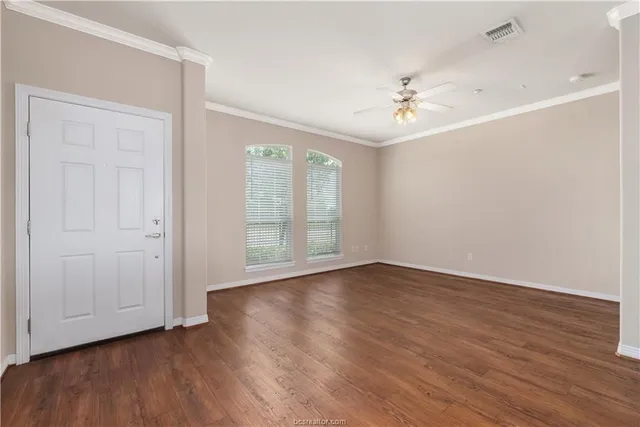 an empty room with wooden floor ceiling fan and windows