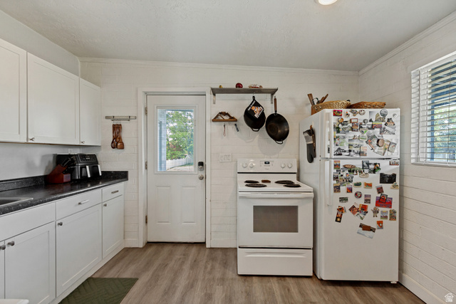 White cabinetry with dark countertops, wood-finish flooring, white appliances, and a glass-paneled door