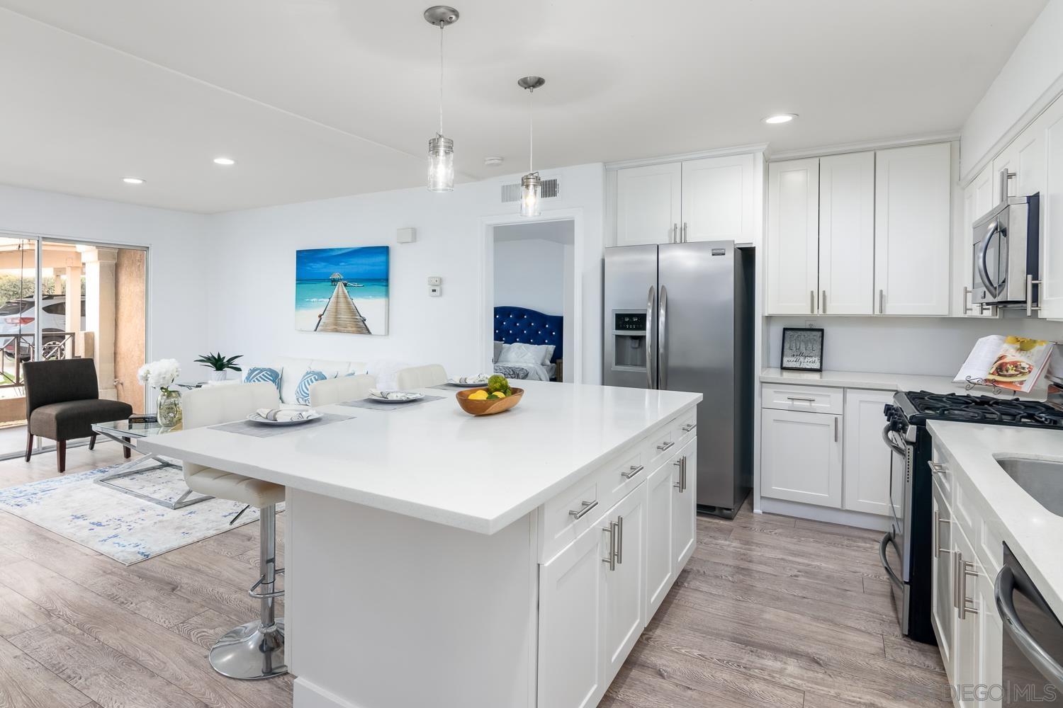 a kitchen with stainless steel appliances kitchen island granite countertop a refrigerator a sink dishwasher a stove with white cabinets and wooden floor