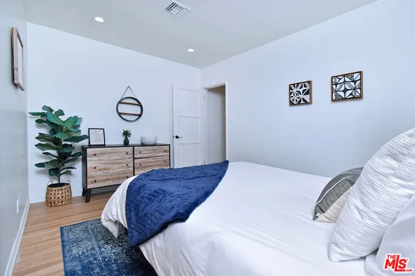 a bedroom with a bed a dresser and potted plants
