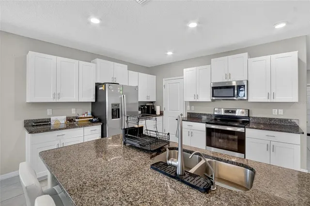 a kitchen with stainless steel appliances granite countertop a sink a stove a refrigerator with white cabinets and wooden floor