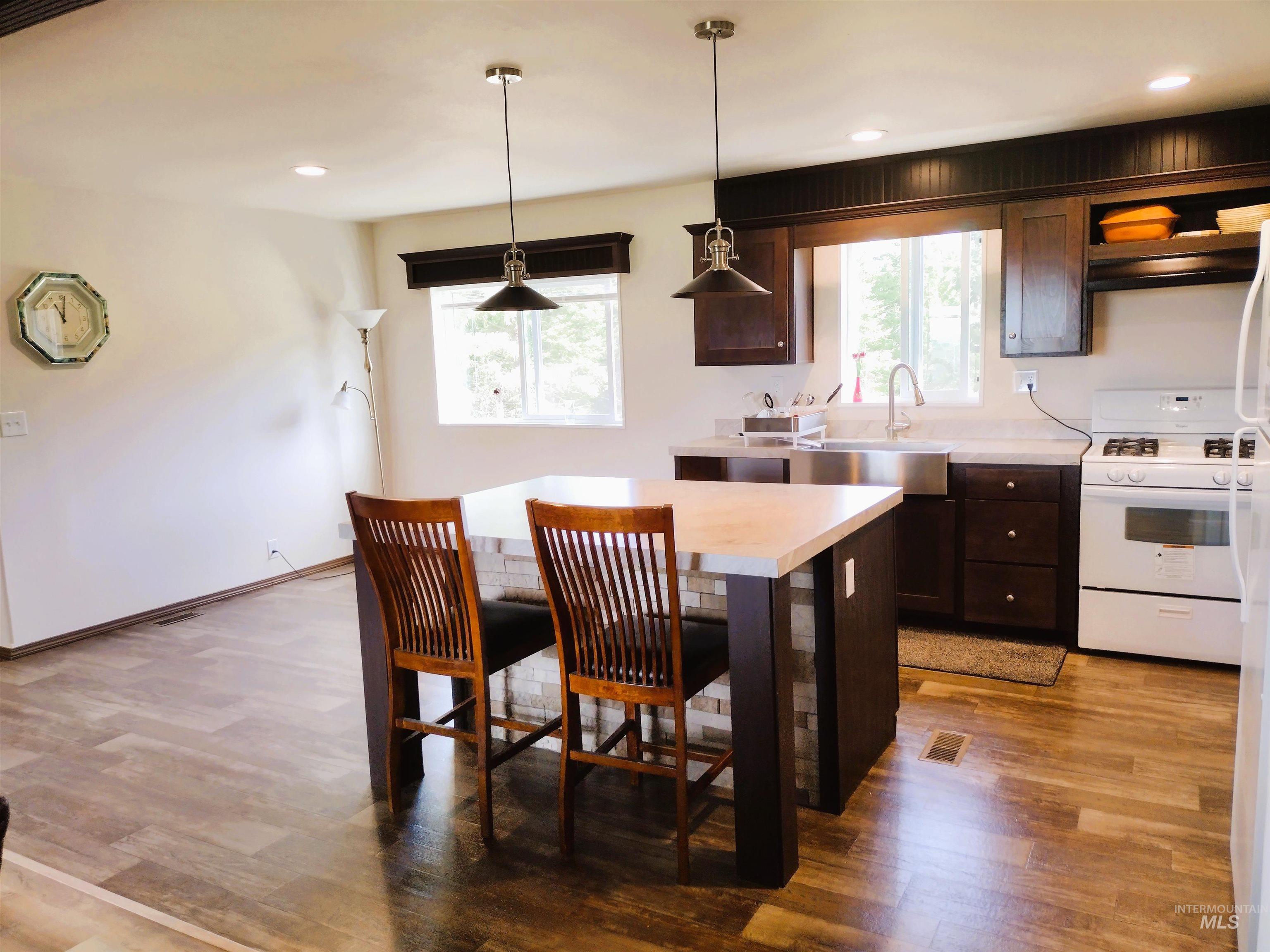 142 Shenandoah Third Street Kamiah, ID 83536 - Photo 26 of 50 Kitchen featuring light countertops, dark wood finish cabinets, white gas range oven, wood finished floors, and a kitchen breakfast bar