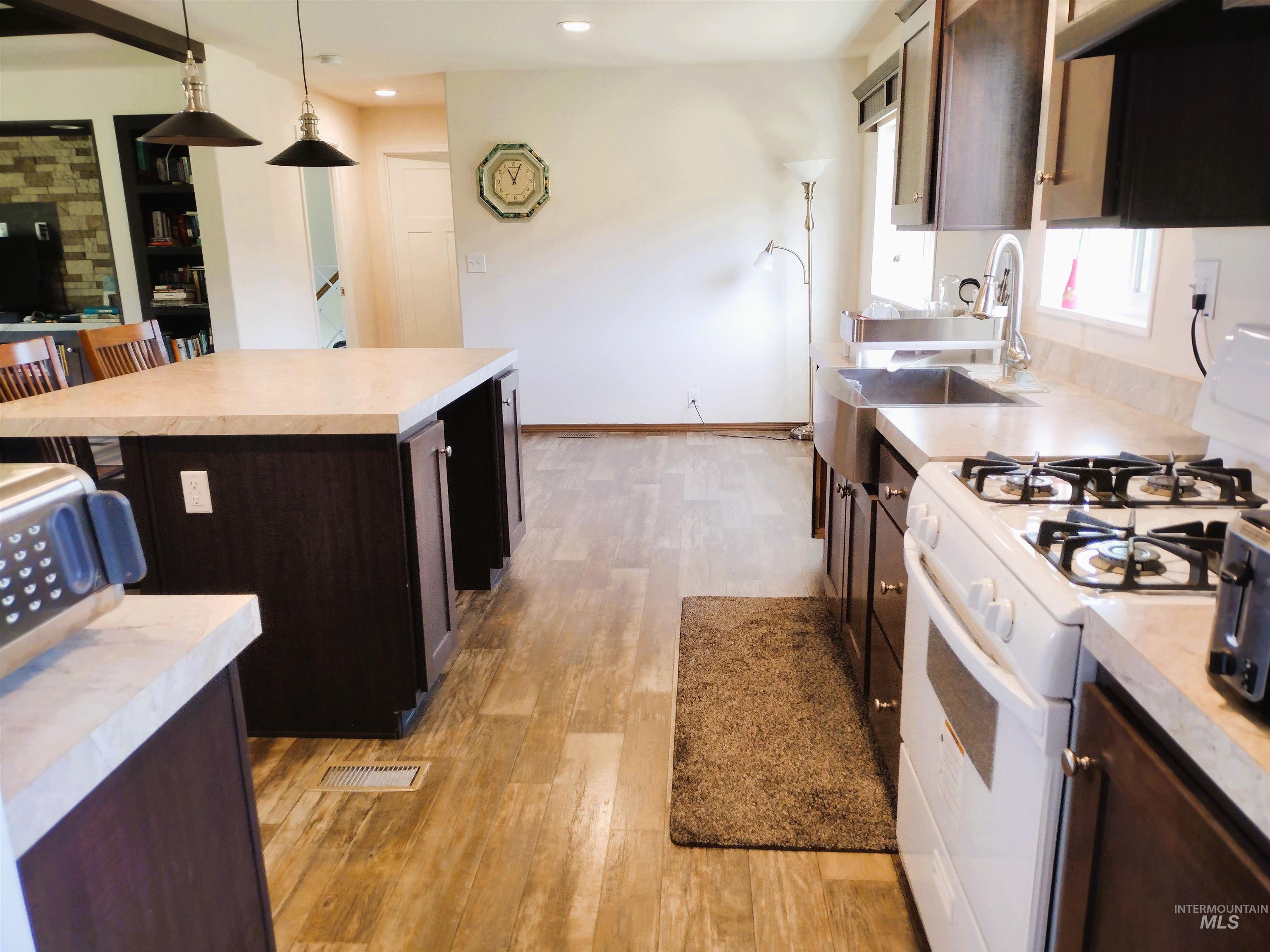 142 Shenandoah Third Street Kamiah, ID 83536 - Photo 29 of 50 Kitchen with white range with gas cooktop, light countertops, dark wood finish cabinets, hanging light fixtures, and light wood finished floors