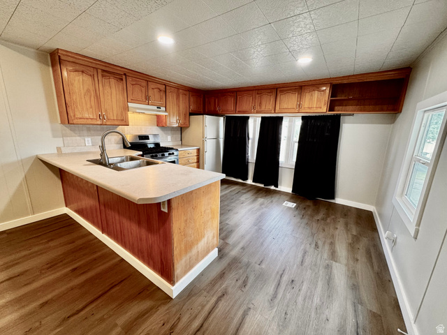 158 Cushing Way Layton, UT 84041 - Photo 4 of 14 Kitchen featuring wood cabinetry, laminate countertops, a stainless steel sink with a gooseneck faucet, a gas range, and wood-finish flooring
