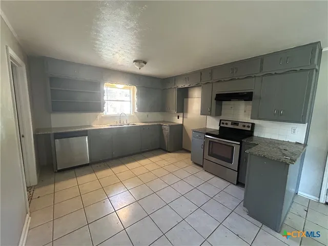 a kitchen with granite countertop a stove a sink and a refrigerator