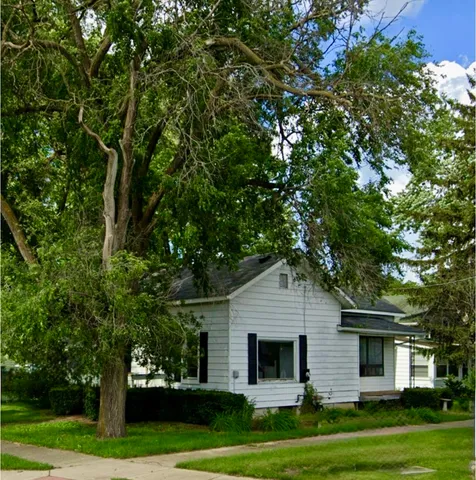 a view of a white house next to a yard with big trees