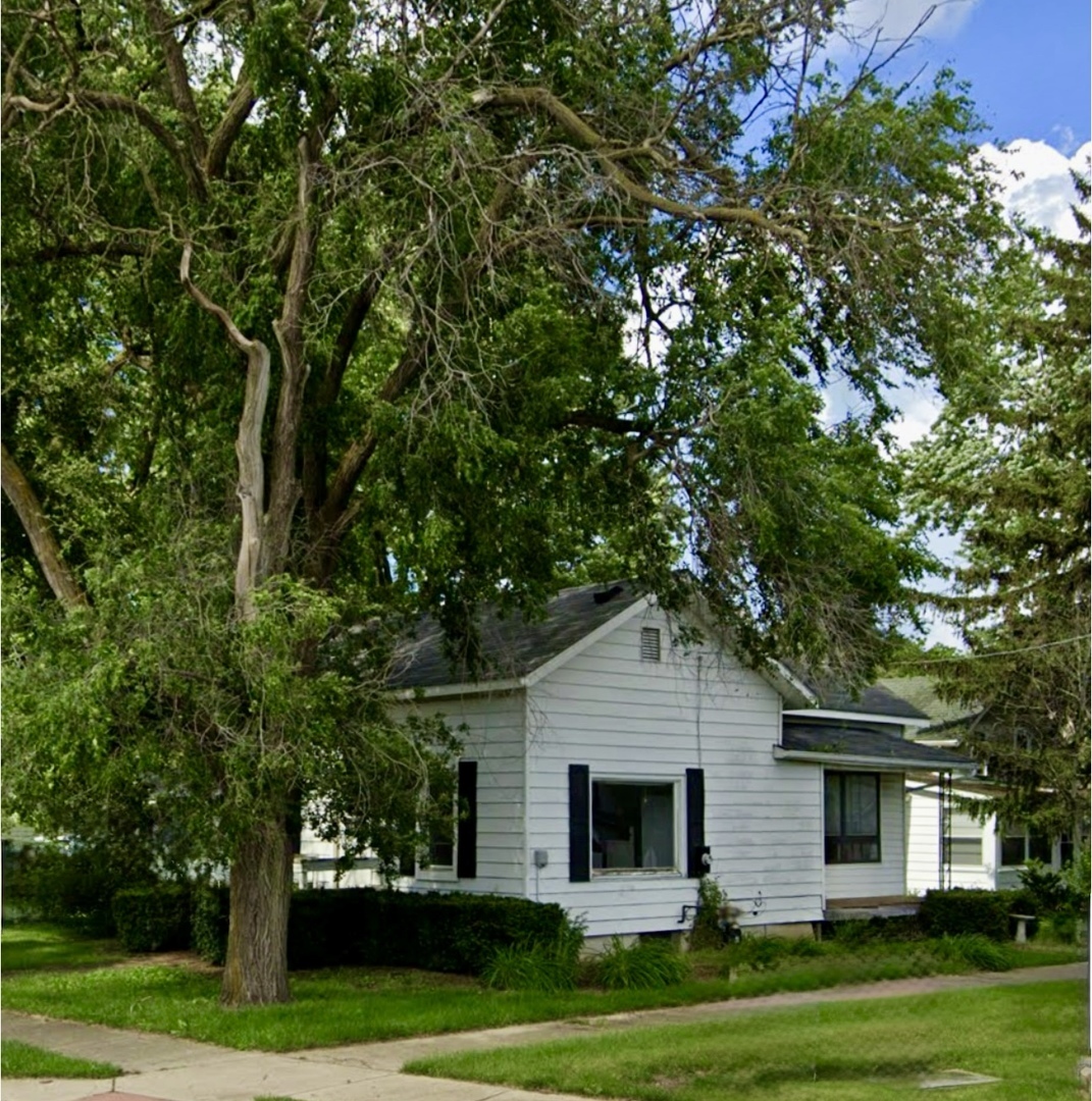 a view of a white house next to a yard with big trees