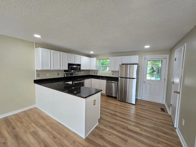 a kitchen with stainless steel appliances granite countertop a refrigerator a sink dishwasher a stove and white countertops with wooden floor