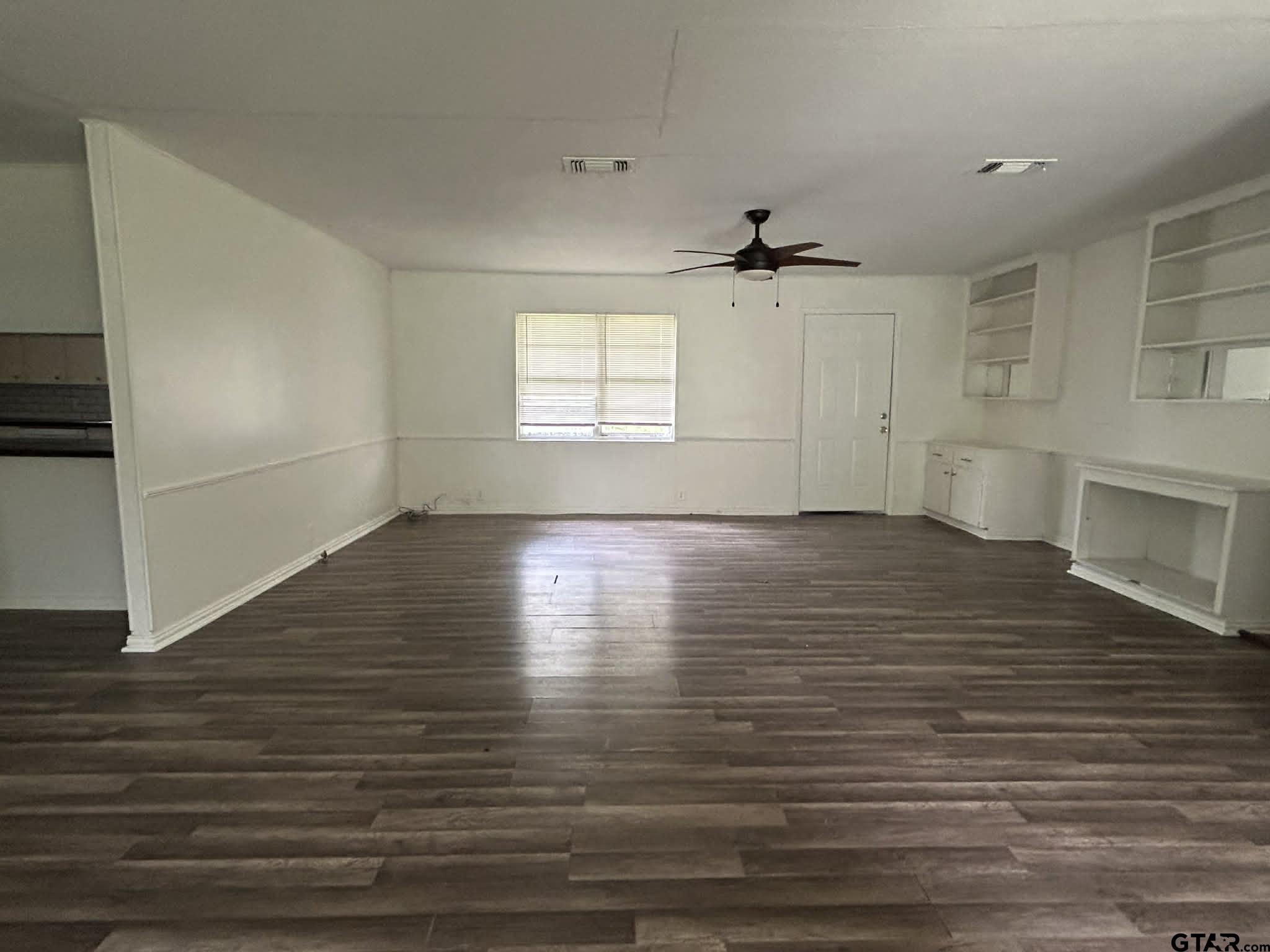 an empty room with wooden floor ceiling fan and windows