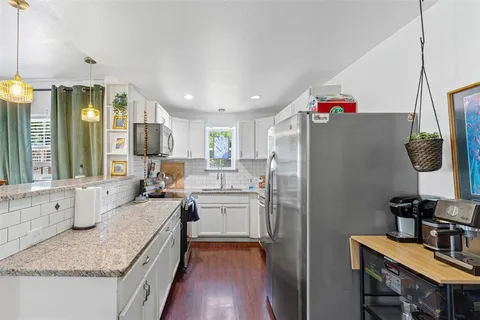 a kitchen with granite countertop a refrigerator a sink dishwasher stove and white cabinets next to a window