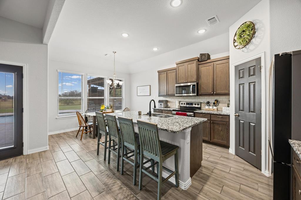 5405 Ranger Drive Midlothian, TX 76065 - Photo 12 of 29 Primary Kitchen with hanging light fixtures, a breakfast bar, a chandelier, light stone countertops, and stainless steel appliances