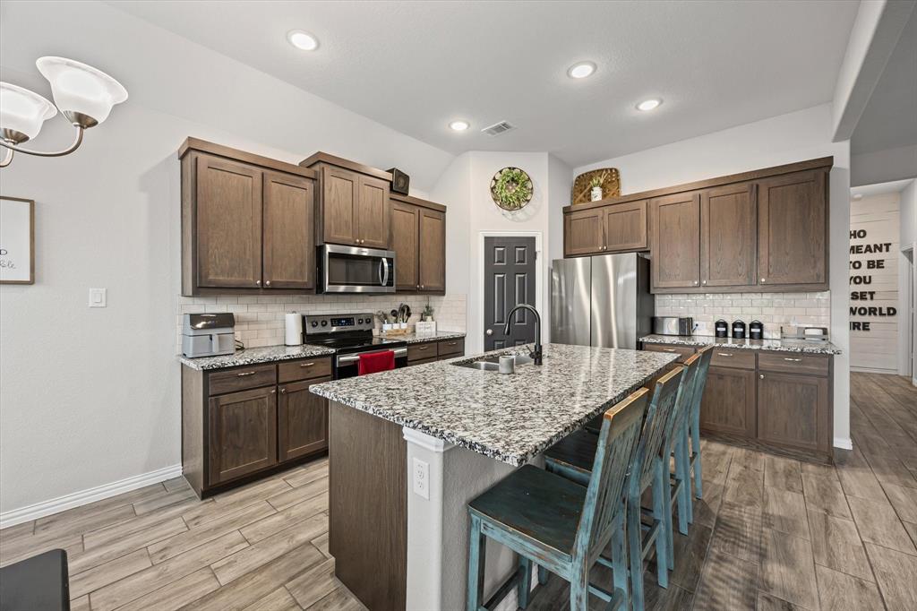5405 Ranger Drive Midlothian, TX 76065 - Photo 13 of 29 Primary Kitchen featuring light stone countertops, appliances with stainless steel finishes, tasteful backsplash, a kitchen bar, and recessed lighting