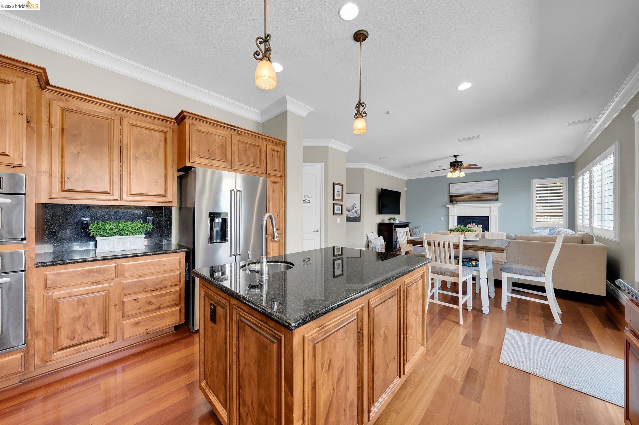 2513 Winged Foot Road Brentwood, CA 94513 - Photo 9 of 45 Open-concept kitchen featuring wood-finish flooring, a central island with a dark countertop and undermount sink, stainless steel appliances, and custom wood cabinetry