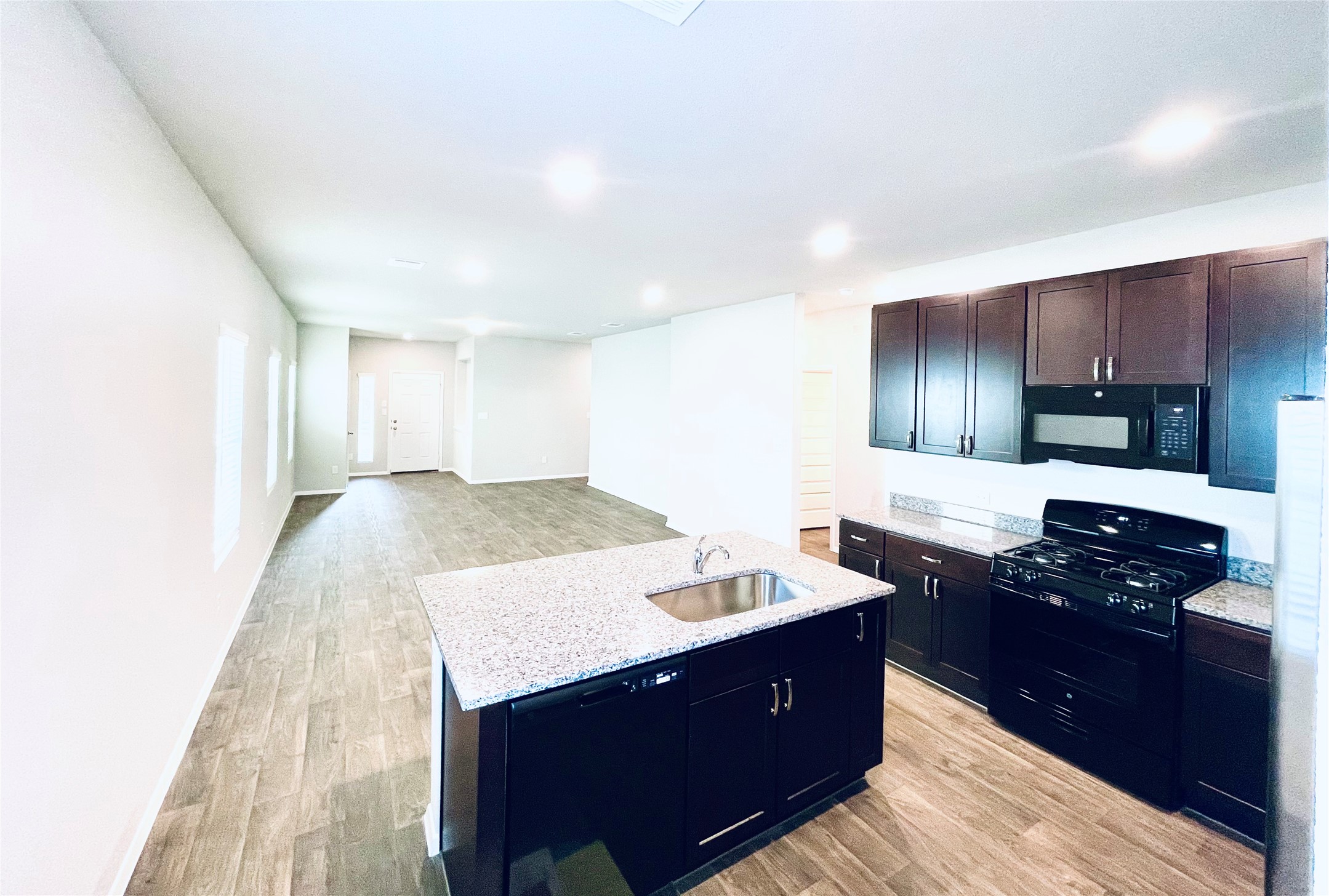 117 Huckleberry Lane Elgin, TX 78621 - Photo 5 of 34 Kitchen with black appliances, a sink, light wood-style floors, and a center island with sink