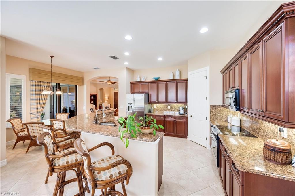 7660 Cottesmore Drive Naples, FL 34113 - Photo 13 of 50 a kitchen with stainless steel appliances kitchen island granite countertop a table chairs and a refrigerator