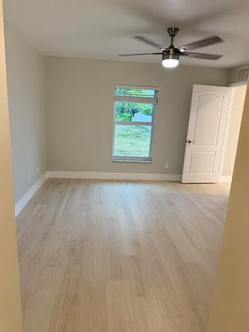 an empty room with wooden floor fan and windows